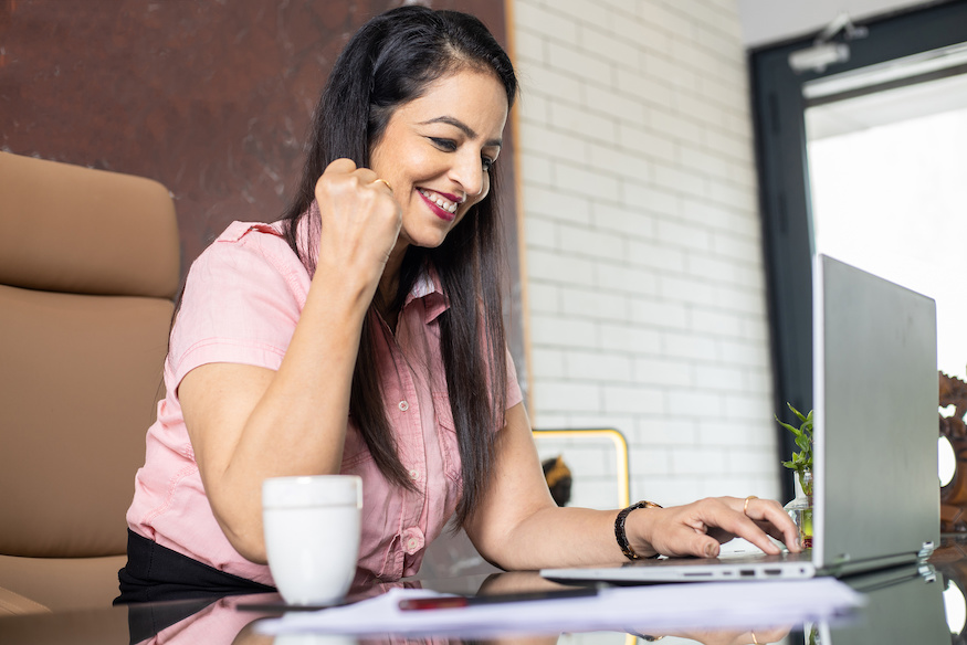 Young happy indian woman entrepreneur working on laptop computer in office.